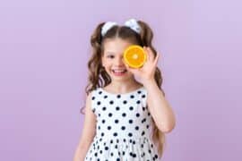 The child covered one eye with an orange. Citrus fruits for children's nutrition.