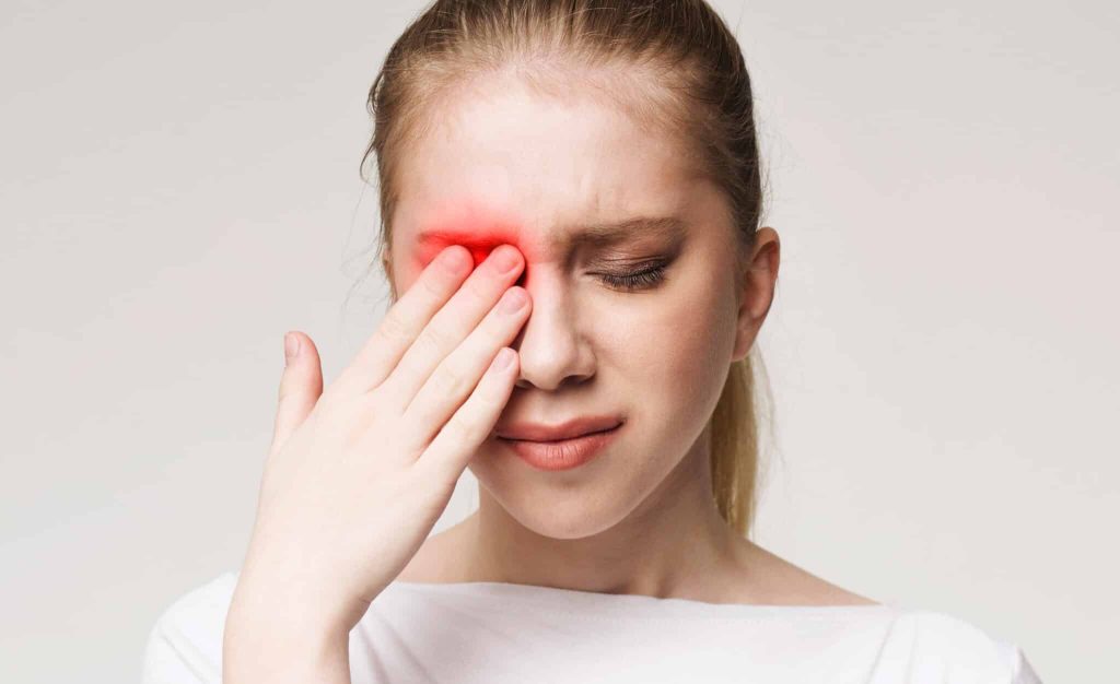 woman holding hand over one eye in discomfort