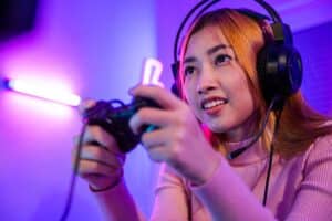 You win. Gamer using joystick controller plays online video game with computer neon lights very determined, woman wear gaming headphones playing