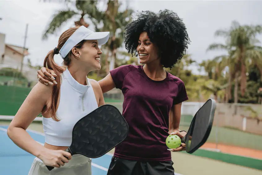 Two women holding pickleball paddles on an outdoor court