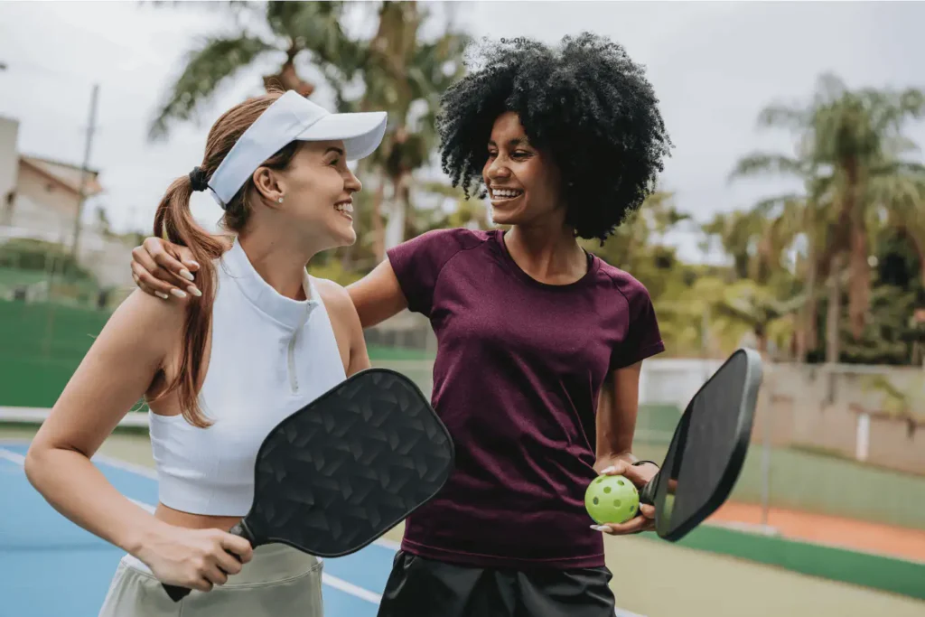 Two women holding pickleball paddles on an outdoor court